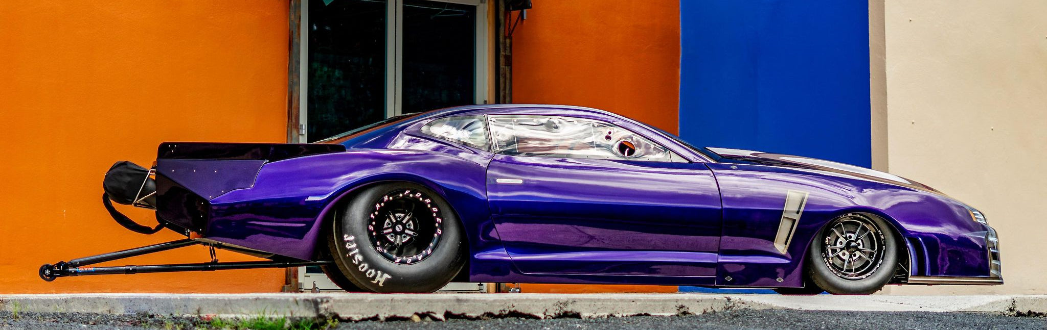 Purple sports car parked in front of a building with an orange wall and blue door.